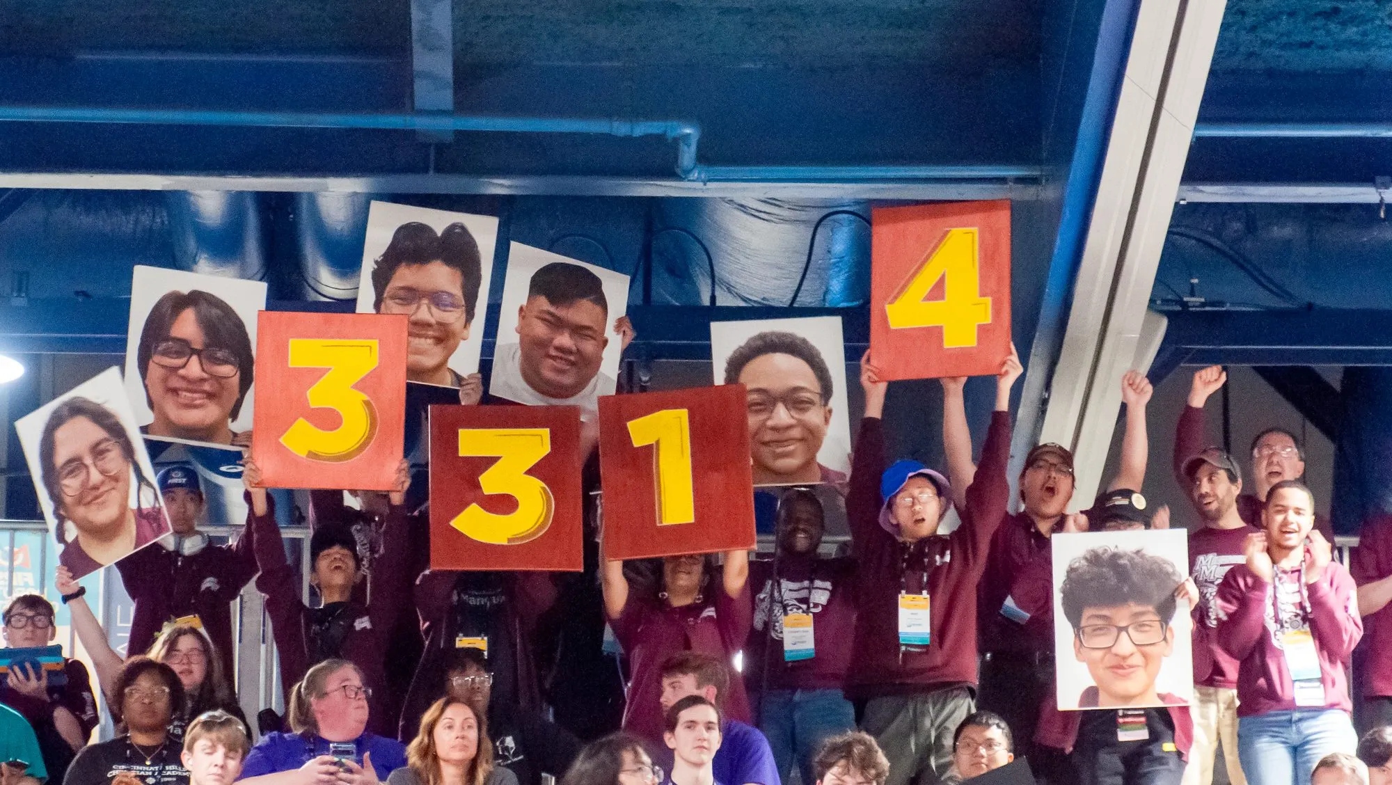 Students in the stands holding up 3314 number signs and teammate face cutouts